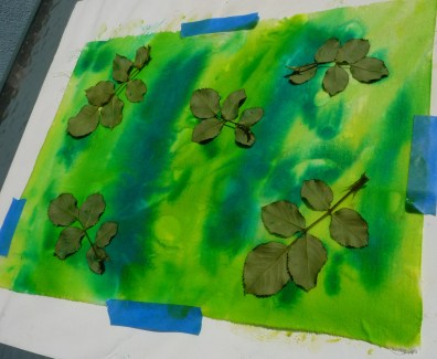 Fresh leaves from a rose bush are arranged on the wet painted surface of the fabric